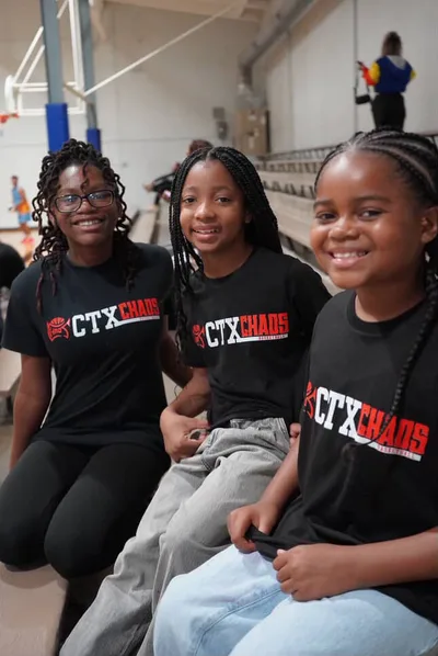 Three young supporters in CTX Chaos shirts at a home game